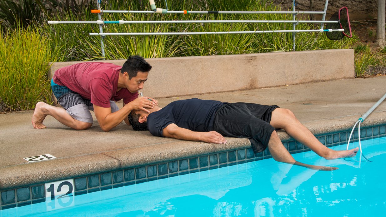 A person performing CPR on another individual who is lying by the edge of a swimming pool.