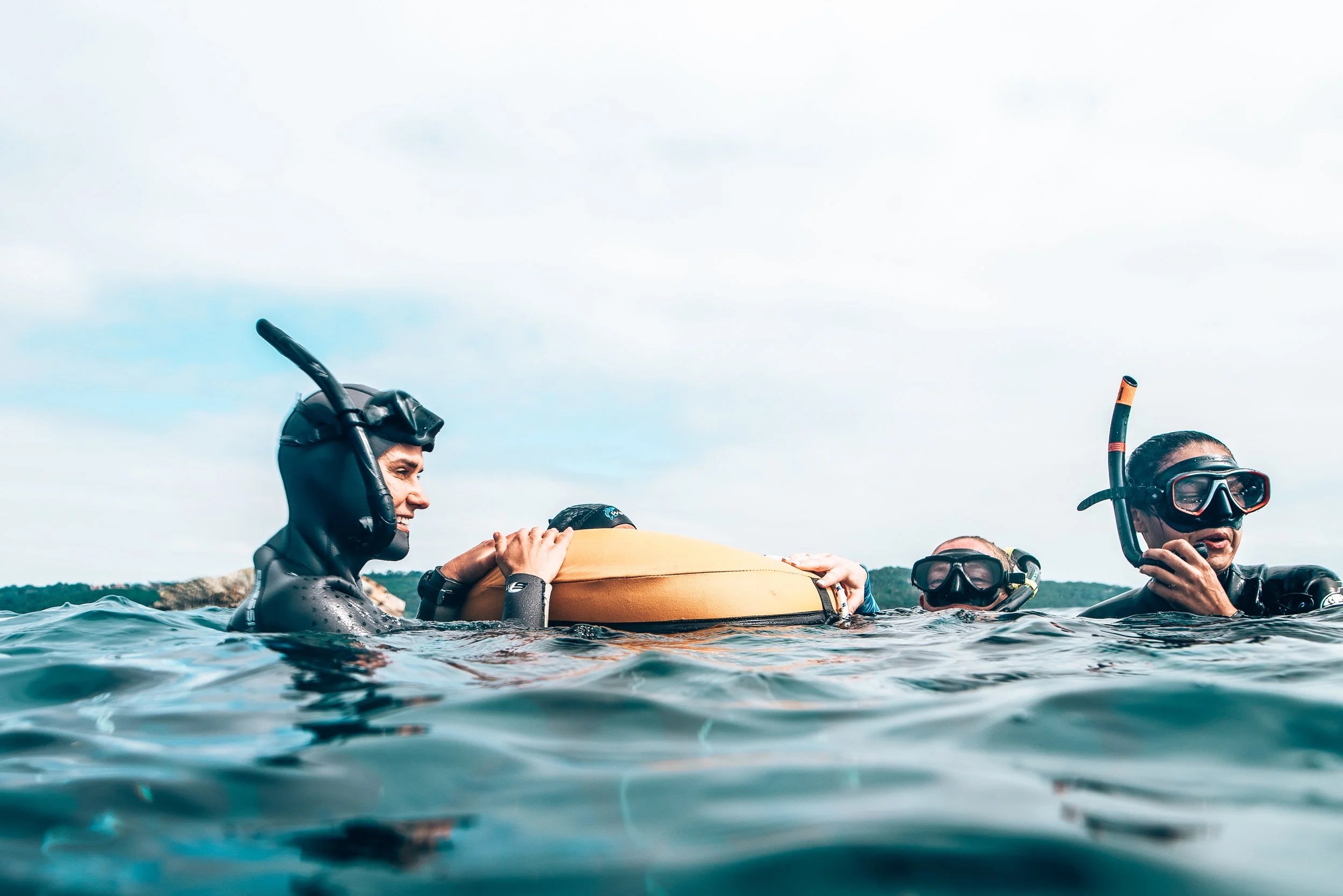 Four individuals in wetsuits and snorkeling gear floating in water, holding onto a flotation device, with one person smiling.