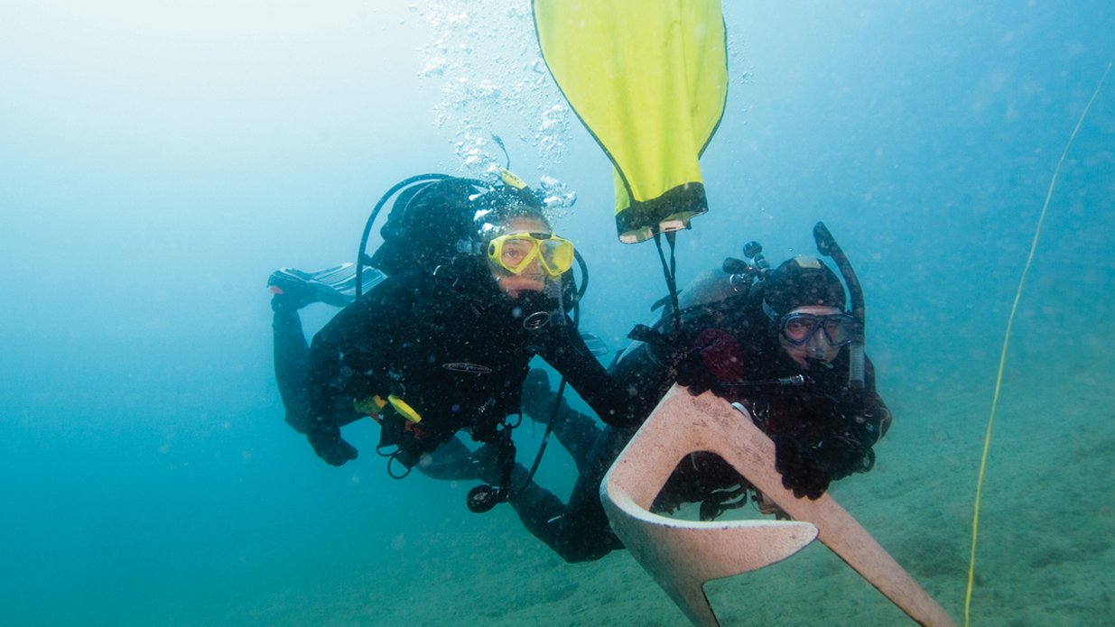 Two scuba divers underwater, one holding a yellow float and the other grasping a piece of equipment.